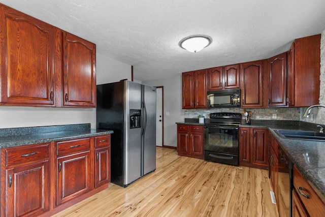 kitchen featuring dark countertops, tasteful backsplash, a sink, black appliances, and light wood-style floors