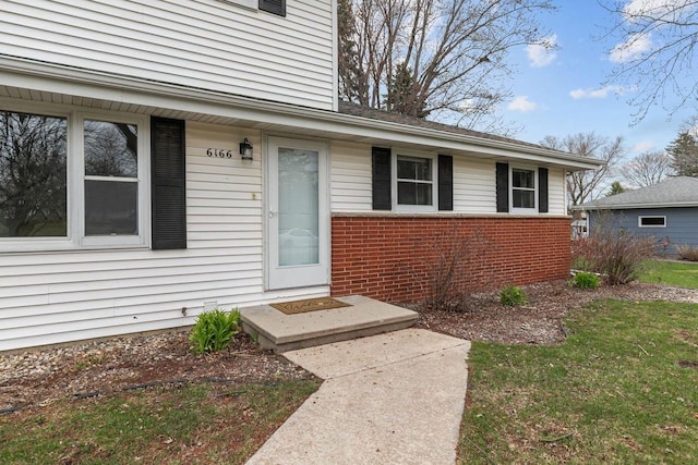 view of exterior entry with brick siding and a lawn