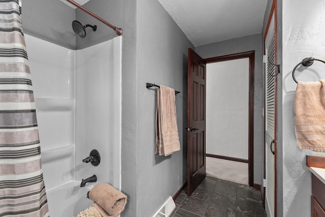 full bath with shower / bath combo, baseboards, stone finish flooring, a textured wall, and vanity