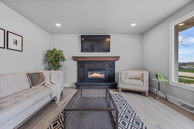 living room with wood finished floors, a glass covered fireplace, baseboards, visible vents, and recessed lighting