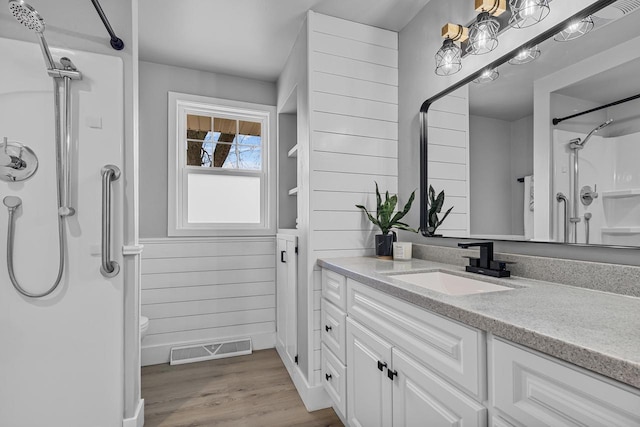 full bathroom featuring wood finished floors, wainscoting, vanity, walk in shower, and visible vents