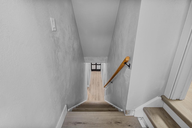 stairway with wood finished floors and a textured wall
