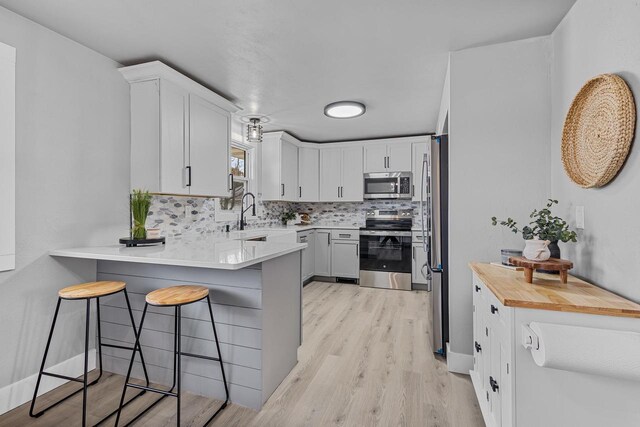 kitchen with stainless steel appliances, a peninsula, a kitchen breakfast bar, light wood-style flooring, and backsplash