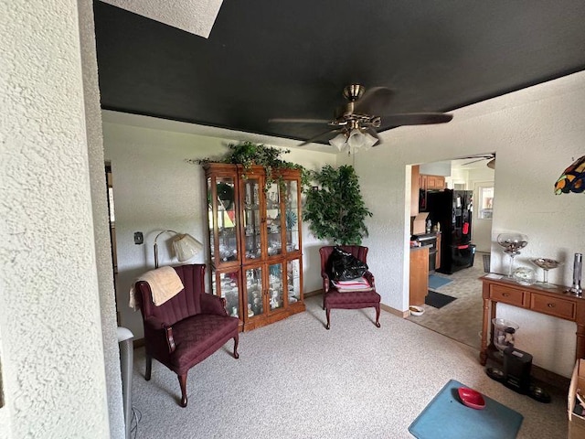 living area featuring baseboards, a textured wall, ceiling fan, and light carpet