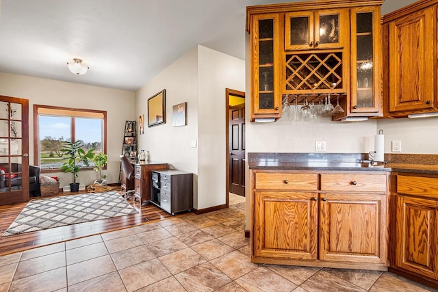 kitchen featuring brown cabinetry, dark countertops, and glass insert cabinets