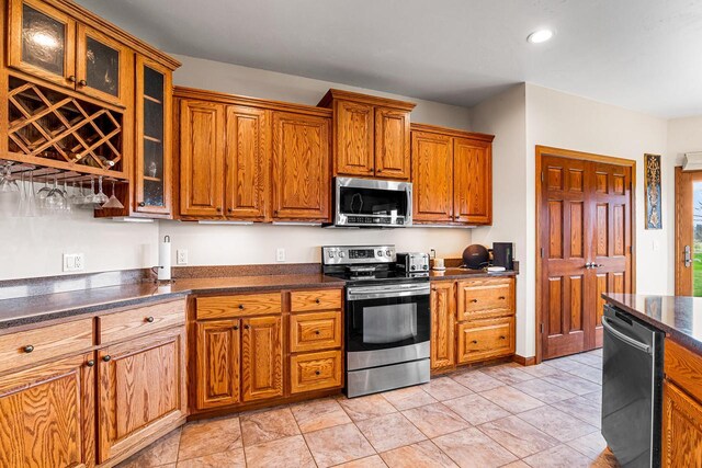 kitchen with brown cabinets, recessed lighting, dark countertops, glass insert cabinets, and appliances with stainless steel finishes