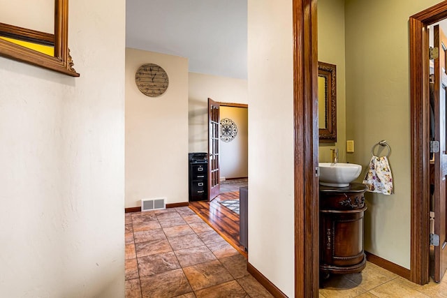 hall with baseboards, a sink, and visible vents