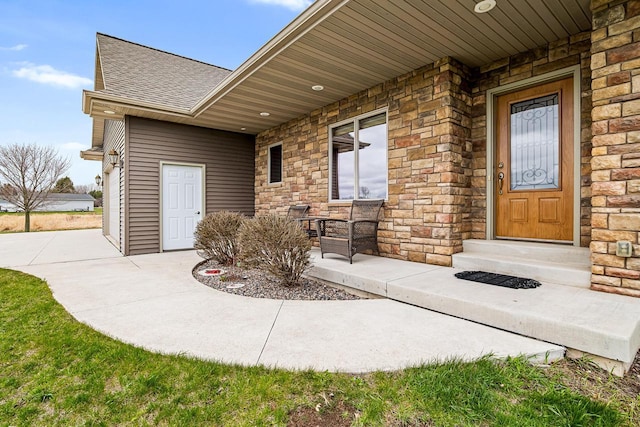 entrance to property featuring stone siding and a shingled roof