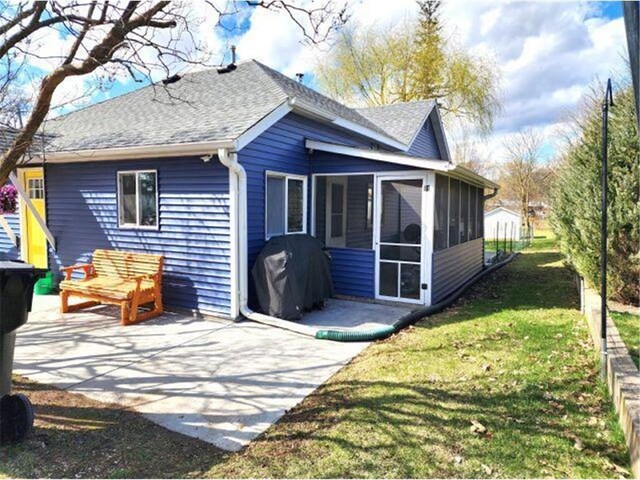 21 N Main St, Luck, WI 54853 - rear view of house with a lawn, a sunroom, a patio area, and a shingled roof