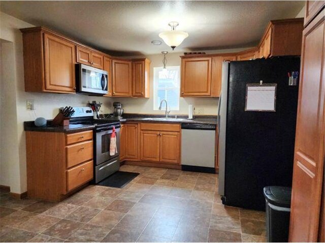 21 N Main St, Luck, WI 54853 - kitchen featuring brown cabinetry, dark countertops, stainless steel appliances, and a sink