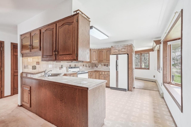 kitchen with decorative backsplash, a peninsula, white appliances, tile counters, and a sink