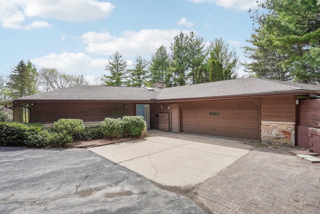 ranch-style home featuring roof with shingles, stone siding, a garage, a chimney, and driveway