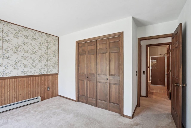 unfurnished bedroom featuring carpet flooring, a baseboard heating unit, wainscoting, and a closet