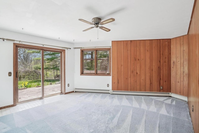 carpeted spare room featuring baseboards, a ceiling fan, a baseboard heating unit, and wooden walls