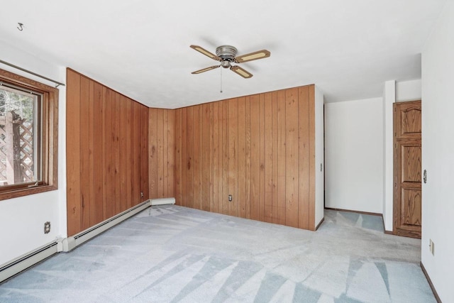 spare room featuring carpet floors, a ceiling fan, baseboard heating, and wood walls