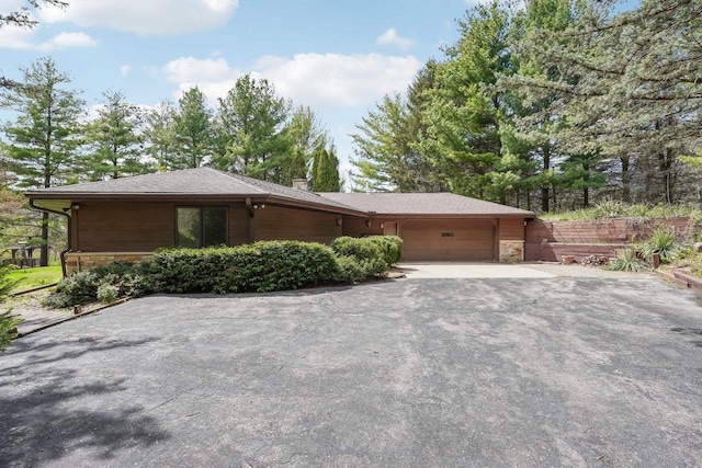 view of front of house with a chimney, a garage, fence, aphalt driveway, and stone siding