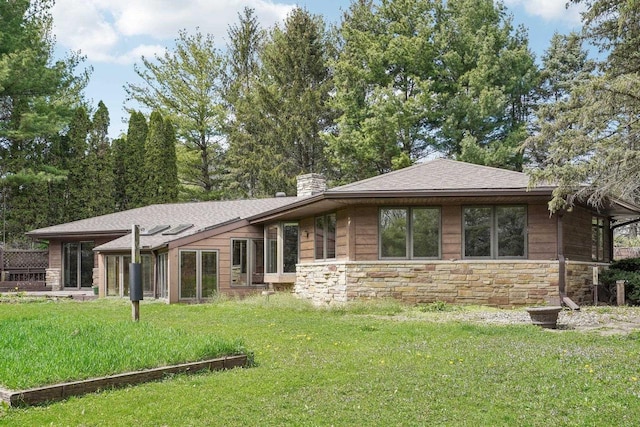 back of house featuring a chimney, a shingled roof, a yard, and stone siding