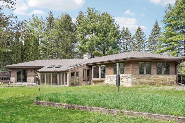 view of front facade with a shingled roof, a chimney, a front lawn, and stone siding