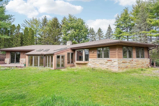 rear view of house featuring a shingled roof, a chimney, a yard, and stone siding