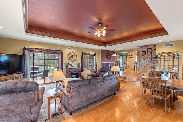 living area featuring recessed lighting, a raised ceiling, light wood-style floors, stairs, and ceiling fan