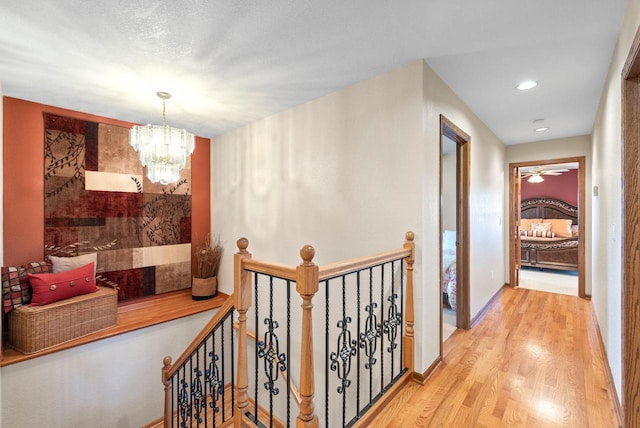 corridor featuring an inviting chandelier, baseboards, wood finished floors, and an upstairs landing