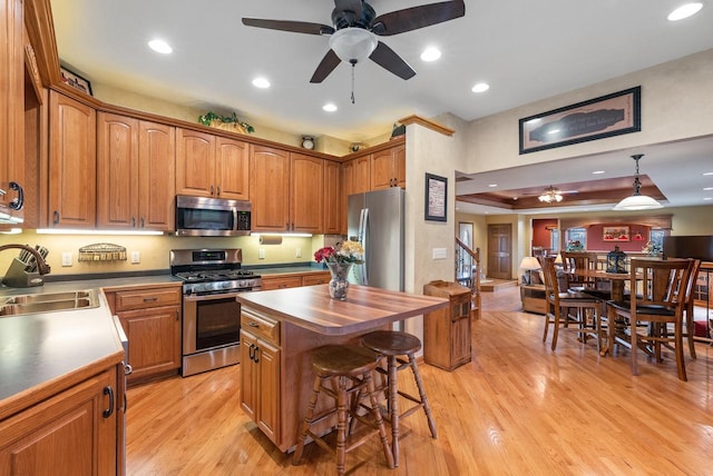 kitchen with a ceiling fan, a kitchen breakfast bar, a sink, light wood finished floors, and appliances with stainless steel finishes