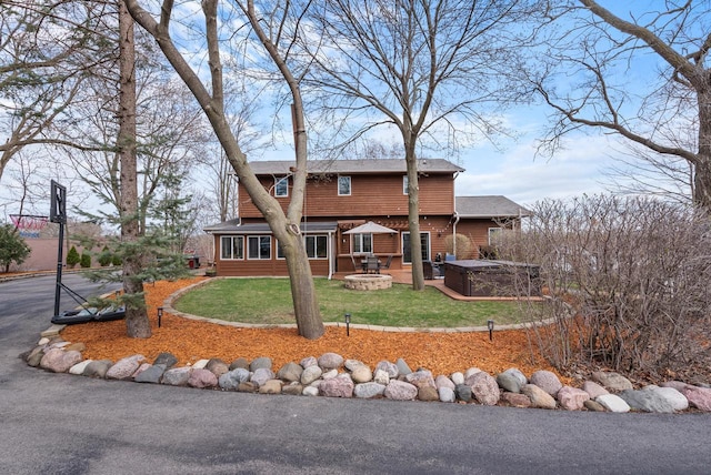 back of property with a shingled roof, a patio, a lawn, a fire pit, and a hot tub