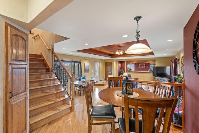 dining area with a ceiling fan, stairs, light wood-style flooring, a raised ceiling, and recessed lighting