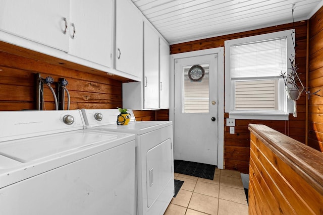 washroom featuring separate washer and dryer, wooden walls, light tile patterned floors, and cabinet space