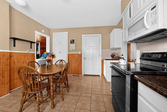 kitchen featuring wooden walls, white microwave, wainscoting, electric range, and white cabinetry