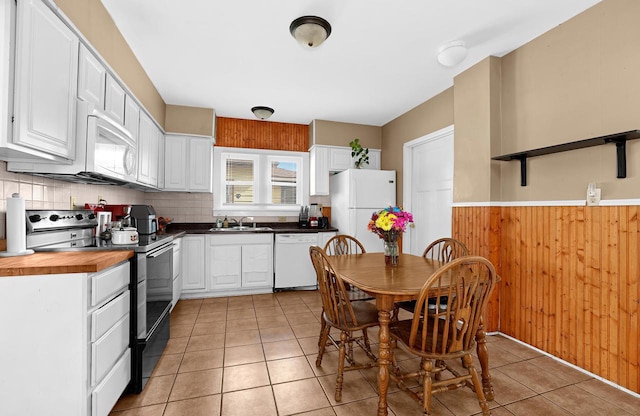 kitchen featuring a sink, wooden walls, white appliances, a wainscoted wall, and white cabinets