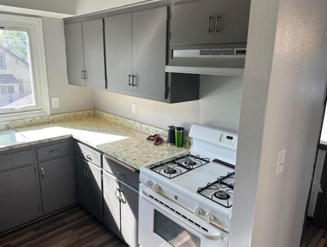 kitchen featuring under cabinet range hood, white range with gas stovetop, gray cabinets, a sink, and dark wood-style flooring