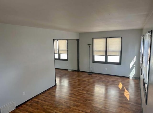 unfurnished room with visible vents, a wealth of natural light, and dark wood-style floors