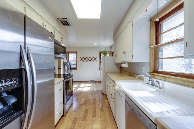 kitchen featuring light wood-style floors, appliances with stainless steel finishes, light countertops, a sink, and white cabinetry