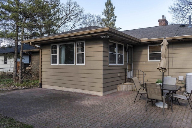 back of property featuring roof with shingles, a chimney, and a patio area