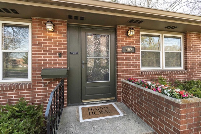 property entrance with covered porch, brick siding, and visible vents