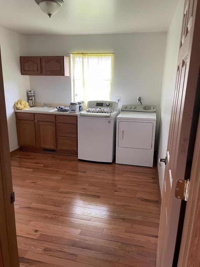 clothes washing area with cabinet space, light wood finished floors, washing machine and clothes dryer, and a sink