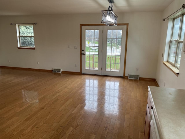 unfurnished dining area featuring wood-type flooring, plenty of natural light, and visible vents