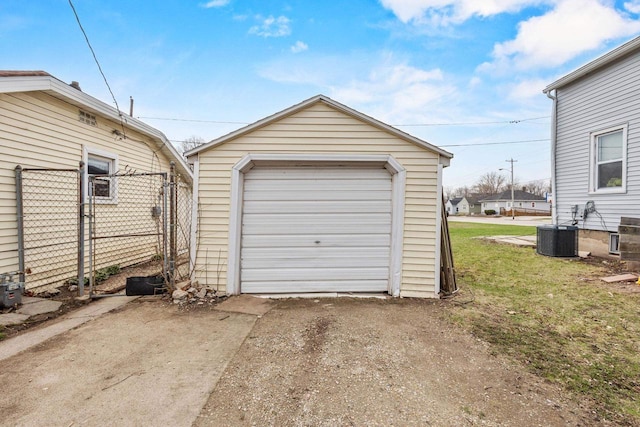 detached garage with driveway, central AC unit, and fence