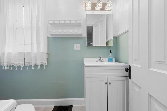 half bathroom featuring visible vents, baseboards, vanity, and toilet