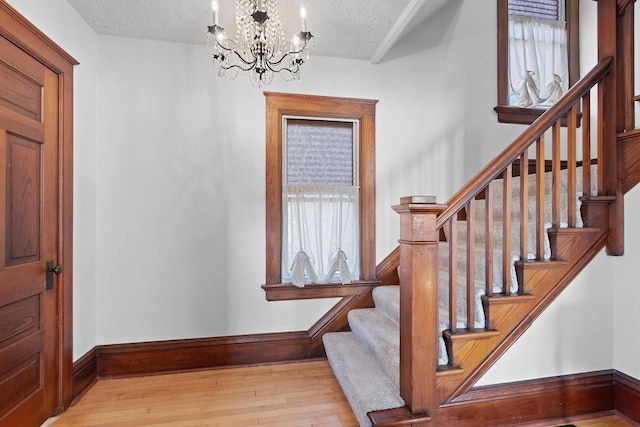 stairway featuring hardwood / wood-style flooring, baseboards, a notable chandelier, and a textured ceiling