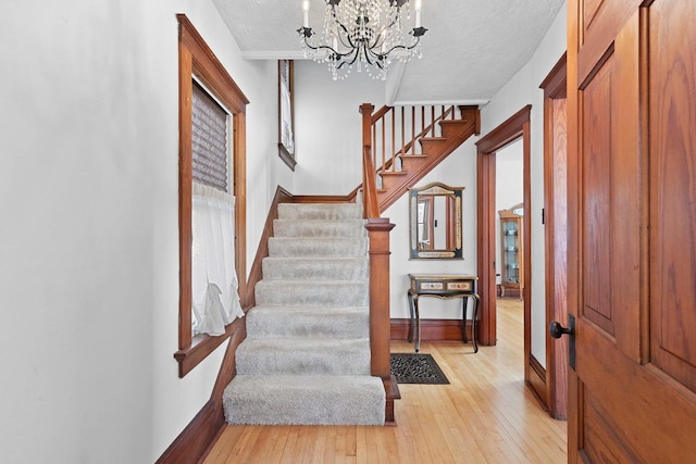 foyer entrance with stairway, light wood finished floors, baseboards, a textured ceiling, and a notable chandelier