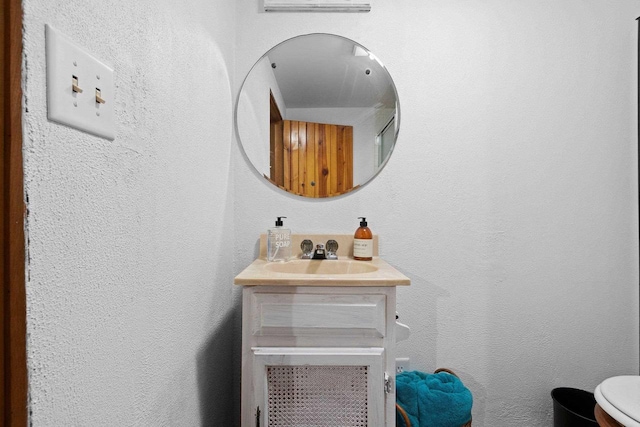 bathroom with a textured wall, vanity, and toilet