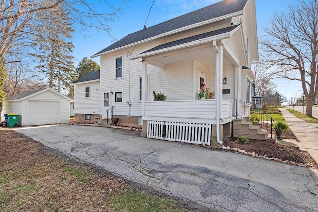 view of side of property with a detached garage, driveway, covered porch, an outbuilding, and roof with shingles