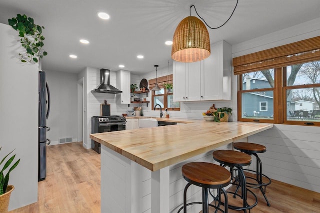 1620 E Murdock Ave, Oshkosh, WI 54901 - kitchen with visible vents, wall chimney exhaust hood, gas range, a peninsula, and wood counters