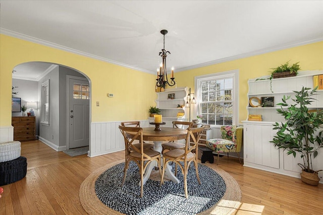 dining space with arched walkways, light wood-style flooring, a wainscoted wall, and ornamental molding
