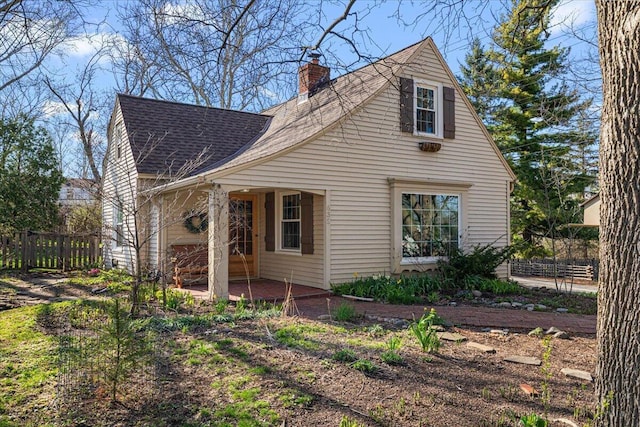 exterior space with fence, a shingled roof, a chimney, and a patio