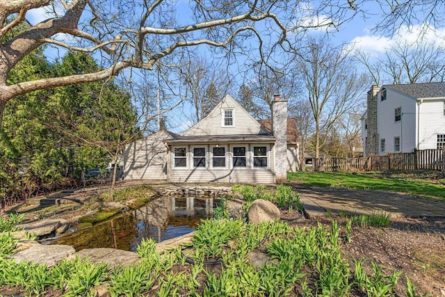 rear view of property with fence, a chimney, and a garden pond