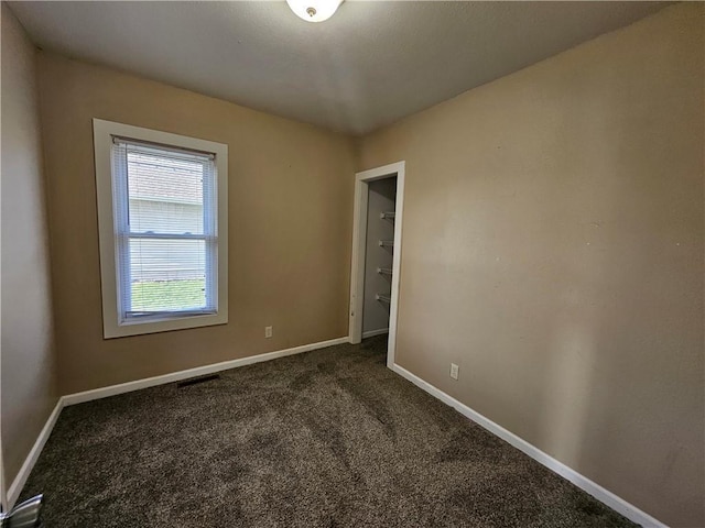 unfurnished room with baseboards, dark carpet, and visible vents