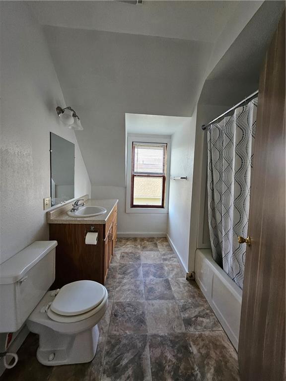 bathroom with stone finish floor, shower / bath combination with curtain, vanity, toilet, and lofted ceiling